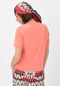 Short-sleeved coral t-shirt made of smooth cotton, paired with patterned pants showcasing geometric shapes in pink, red, and black.