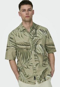 Korte mouwen hemd in lichtgroen met een bladerenpatroon. Gemaakt van stof met een geweven structuur, met een knoopsluiting aan de voorkant en een borstzakje.
