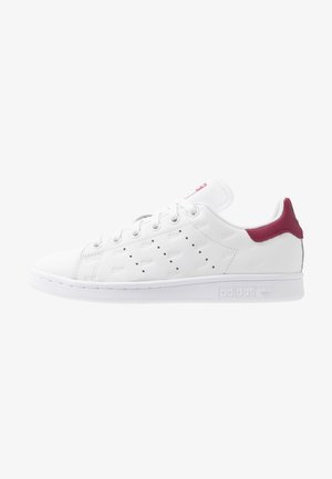 White leather sneaker featuring a maroon heel tab, perforated detailing, and textured accents, with a smooth rubber sole and branding.