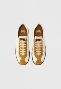 Par vita vita och beige sneakers i campingstil med snören, bruna sulor och "Pelotas Camper" tryckt på insidan.