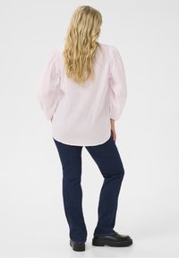 Jasnoróżowa bluzka z bufiastymi rękawami o teksturowanym wykończeniu, w połączeniu z ciemnoniebieskimi prostymi dżinsami i czarnymi butami na platformie.
