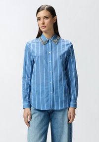 Camicia a righe blu chiaro con colletto decorativo in perline. Presenta una chiusura button-down e maniche lunghe. Realizzata in tessuto liscio.