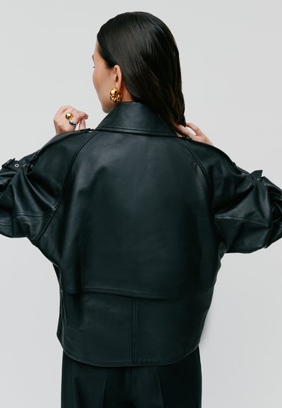 Giubbotto di pelle nera con un design corto, spalle larghe e una texture liscia. Le caratteristiche includono un colletto alto e cuciture minime.