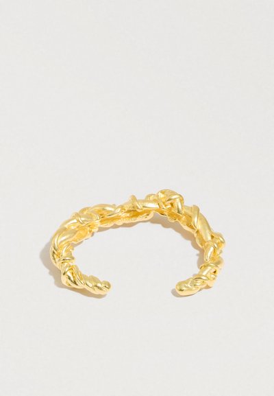 Anel de metal dourado torcido com design aberto, apresentando uma superfície texturizada e padrões entrelaçados.