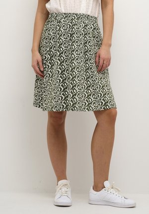 Jupe verte avec un motif abstrait blanc, taille élastique, longueur genou, fabriquée en tissu léger, associée à des baskets blanches.