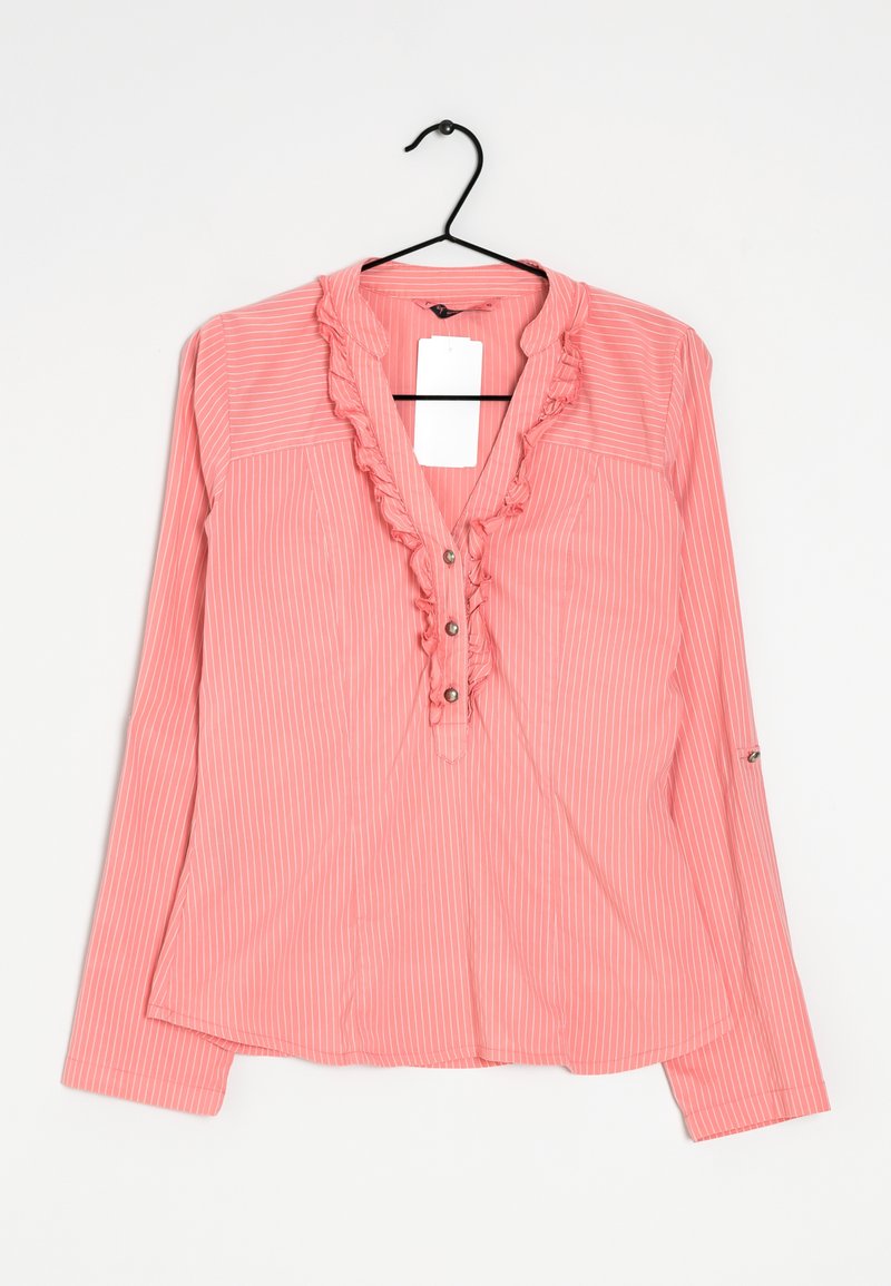 Blouse rose à manches longues avec des rayures verticales blanches, col en V volanté, boutons et une étiquette blanche, suspendue sur un cintre noir sur fond blanc.