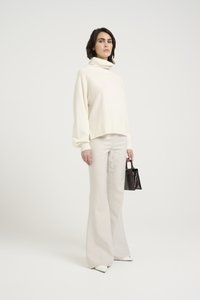Overdimensjonert kremfarget genser med høy krage, sammen med lyse beige flagrende bukser. Svart håndveske med en strukturert design og hvite spisse sko.