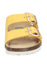 Gele leren slipper met twee verstelbare metalen gespen, kurken voetbed en een witte rubberen buitenzool met een gestructureerd patroon.