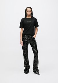 Sort bomulls-T-skjorte med «PINKO»-logo, kombinert med skinnende svarte skinnbukser i falskt skinn. Buksene har en løs passform og innsvingt ben.