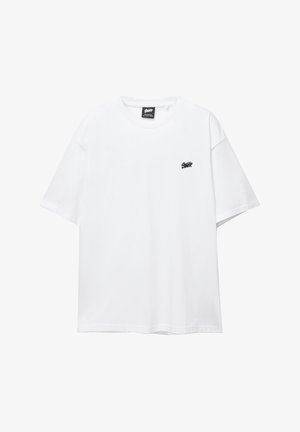 Bijela pamučna majica s kratkim rukavima, okruglim izrezom i malim crnim logom na prsima. Glatka tekstura i ležeran kroj.