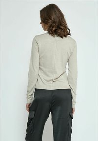 Maglione beige chiaro con maniche lunghe, orlo a costine e dettaglio della cucitura al centro della schiena, abbinato a pantaloni cargo neri con tasche laterali.
