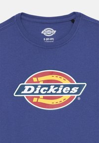 Mėlynas medvilninis marškinėliai su apvaliu iškirpimu. Viduryje yra didelis, daugiakanalis "Dickies" logotipas, o rankovės yra trumpos.