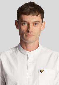 Camicia bianca con colletto, caratterizzata da un design con bottoni e un piccolo logo ricamato sul taschino sinistro. Tessuto di cotone liscio.