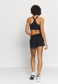 Svart sportbh med racerback-design, kombinerad med svarta träningsshorts och ljusblå löparskor. Slät tygkvalitet och minimala varumärkesdetaljer.
