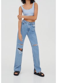 Top corto a coste di colore azzurro chiaro, abbinato a jeans in denim chiaro con grandi strappi sulle ginocchia e design a gamba dritta, completato da sandali neri.