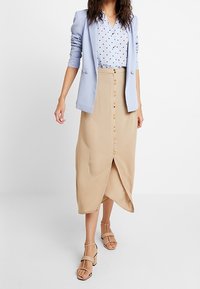 Ljusblå kavaj över en prickig skjorta, beige knäppfront midi-kjol med en framspricka, tillsammans med strappy sandaler i nudefärg.