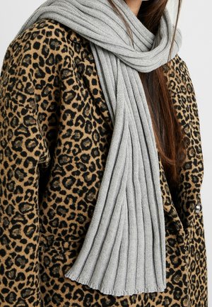 Femme portant un manteau imprimé léopard beige et noir avec une longue écharpe côtelée gris clair enroulée autour du cou.