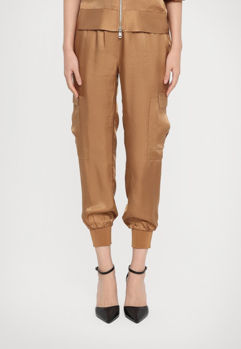 Satijnen cargo-broek in een warme bruine kleur, met elastische boorden, zijzakken en een relaxte pasvorm, gecombineerd met zwarte pumps met een spitse neus.