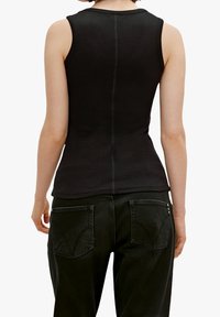 Top sin mangas negro de canalé con un diseño ajustado, que presenta un cuello redondo y detalles de costura vertical en la parte posterior. Combinado con jeans oscuros.