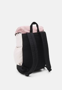 Sac à dos avec un dessus en tissu rose, des sangles noires et un corps texturé noir avec un accent crème clair. Sangles réglables et petites poches latérales.