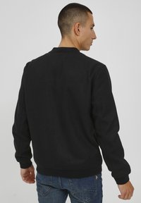 Svart hettegenser med rund hals og lange ermer, laget av et mykt, teksturert materiale. Har ribbestrikkede mansjetter og nederkant.