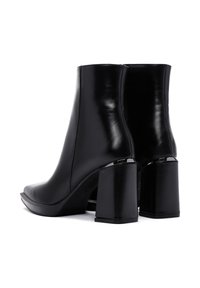 Botas de tobillo de cuero negro con un acabado suave, punta cuadrada y tacones gruesos. Detalle de cremallera en la parte trasera y una silueta elegante.
