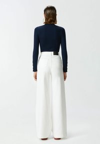 Top a maniche lunghe a coste blu navy abbinato a pantaloni bianchi a vita alta e a gamba larga. I pantaloni presentano tasche posteriori e un dettaglio in pelle in vita.