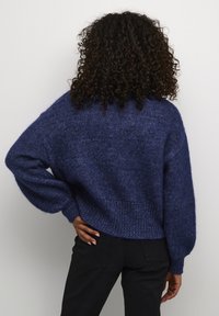 Pulover tricotat de culoare bleumarin, cu un croi lejer, umeri lăsați și material texturat. Prezintă mansete și tiv cu model în bucle, oferind o siluetă relaxată.