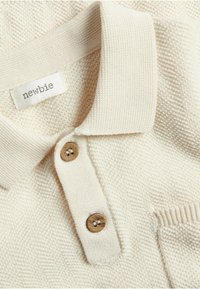 Cremfarbener Poloshirt aus strukturiertem Stoff, mit geripptem Kragen, zwei Holzknöpfen und einer kleinen Brusttasche.
