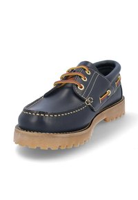 Zapato de barco de cuero marino con suela de goma marrón claro, costuras en contraste y ojales dorados. Presenta cordones en una combinación de colores marrón claro y naranja.