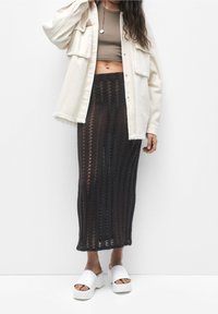 Czarna, dziana spódnica do ziemi w pionowe paski, zestawiona z krótka beżową bluzką i dużą kremową kurtką. Białe sandały na platformie.