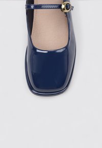 Zapato Mary Jane de charol azul marino con punta redondeada, tira al tobillo y detalle de hebilla en tono dorado. Textura suave, suela plana.