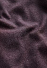 Lilla stof med en glat tekstur, der har folder og krøller, og viser en dyb nuance og et fint strikkemønster.