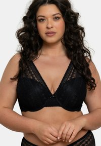 Soutien-gorge en dentelle noire avec un décolleté en V profond, un motif géométrique, des bretelles larges et un petit nœud accent au centre.