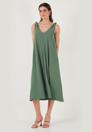Green, sleeveless dress with a V-neck, relaxed fit, and tie details on shoulder straps. Mid-length, smooth fabric with a slight sheen.