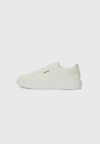 Sneaker bianca a basso profilo con design a lacci, pannello laterale texturizzato e suola spessa, mostrata di profilo su sfondo neutro.