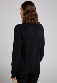 Pull noir tricoté avec un col rond, des manches longues et une base légèrement raccourcie à l'arrière. Texture douce avec un motif en tricot côtelé.