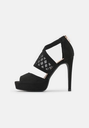 Czarne sandały na wysokim obcasie z otwartym palcem, zamszowy materiał, panel siatkowy w kratkę oraz zamek błyskawiczny z tyłu.