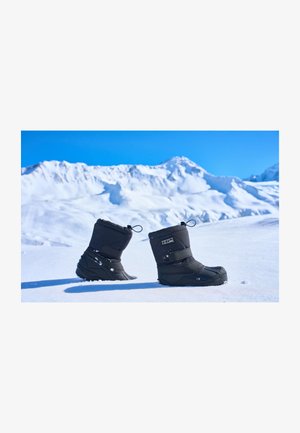 Fekete szigetelt hócipő, párnázott felső résszel, állítható tetejével, texturált gumitalppal és hómotívumokkal, havas hegyvidéki háttér előtt.