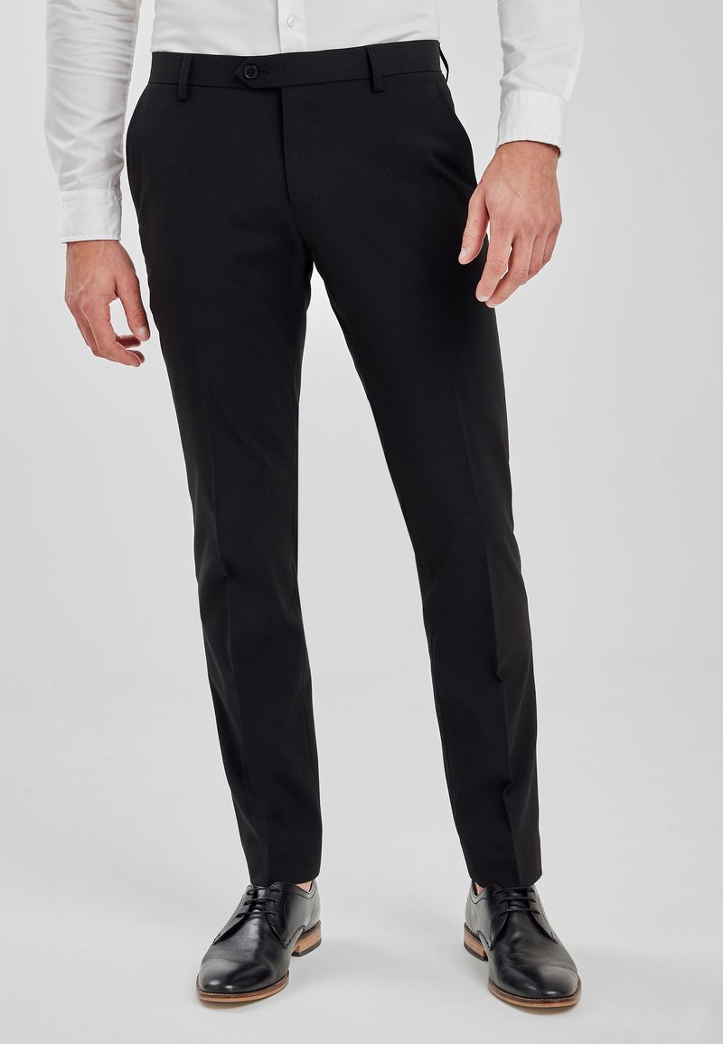 Schwarze maßgeschneiderte Hose mit geradem Schnitt, ausgestattet mit einem vorderen Knopfverschluss und seitlichen Taschen, kombiniert mit schwarzen Lederschuhen.
