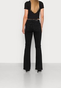 Svarta utsvängda jeans med slim fit och fem fickor, tillverkade av denim. Bärs med en svart kortärmad topp med vågiga ärmar.