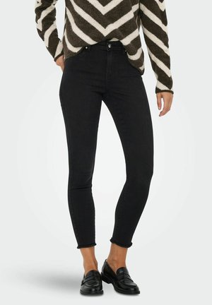 Svarta smala jeans med hög midja, med fransade anklar. Kombinationen med en randig tröja i brunt och creme samt svarta loafers.