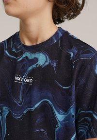 Tricou negru cu mânecă scurtă, având un model marmorat în nuanțe de albastru și teal, cu un logo alb „NXT GRID” pe partea din față.