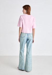 Roze cropped trui met geribbelde textuur, gecombineerd met lichtblauwe flared jeans met bloemenborduursels op de achterzakken.