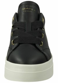 Black leather sneakers with gold hardware, featuring a round toe, thick white rubber sole, and flat black laces. Brand logo embossed on heel.