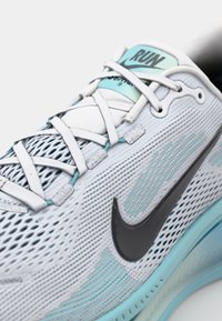 Ľahká bežecká obuv s priedušným bielym sieťovaným zvrškom, čiernym logom Nike a tyrkysovými akcentmi na podrážke a šnurovacom systéme.