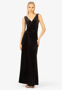 Abito in velluto nero con scollatura a V, senza maniche, busto arricciato e dettaglio drappeggiato. Lungo fino al pavimento con una leggera silhouette ad A.