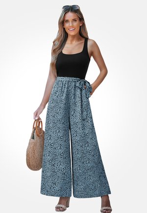 Blauwe wijde broek met zwart gespetterd patroon en een gestrikte taille. Gepaard met een zwarte tanktop en een bruine gevlochten tas.