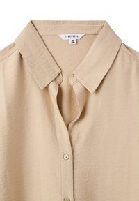 Camicia color beige chiaro con colletto e chiusura con bottoni. Realizzata in tessuto morbido, presenta cuciture visibili e una vestibilità rilassata. Etichetta del brand: Terranova.