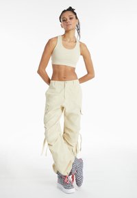 Lys beige avkortet sports-bh, matchende cargo-bukser med lommer, og høy-top svarte og hvite rutete sneakers med rosa snører.